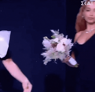 A Woman In A Black Dress Is Holding A Bouquet Of Flowers In Her Hand GIF