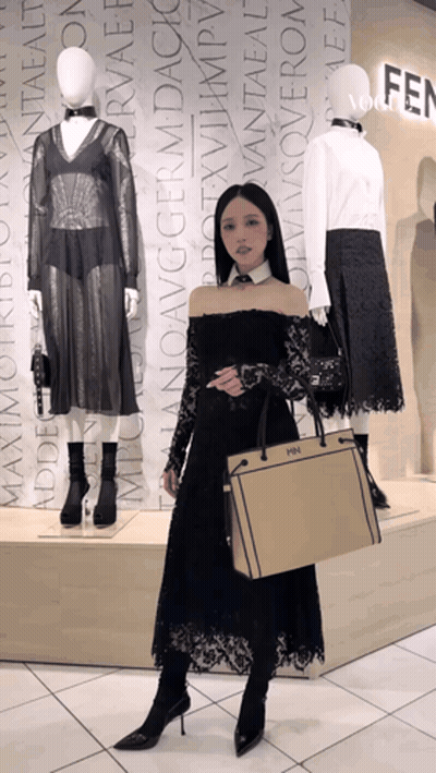 A Woman In A Black Dress Is Holding A Fendi Bag In Front Of Mannequins GIF