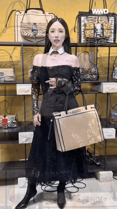 A Woman In A Black Dress Is Holding A Fendi Purse GIF
