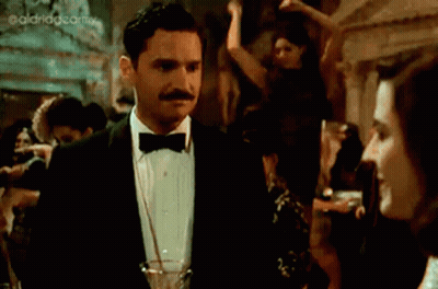 A Woman In A Black Dress Is Holding A Glass Of Champagne GIF