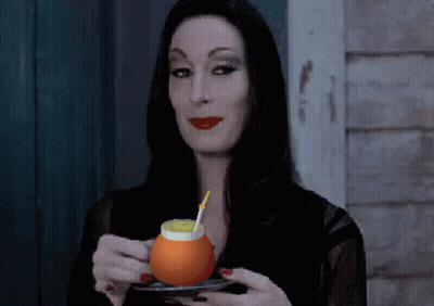 A Woman In A Black Dress Is Holding A Glass Of Orange Juice With A Straw GIF