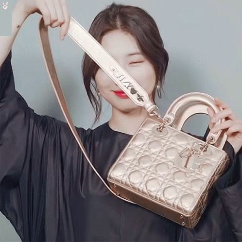 A Woman In A Black Dress Is Holding A Gold Bag With A Strap That Says " I Love You " GIF