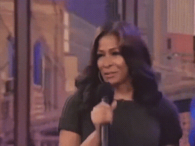 A Woman In A Black Dress Is Holding A Microphone GIF