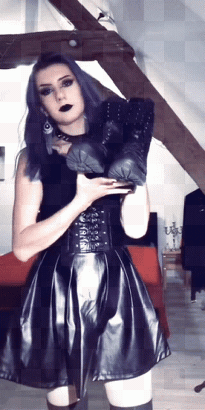 A Woman In A Black Dress Is Holding A Pair Of Black Boots GIF