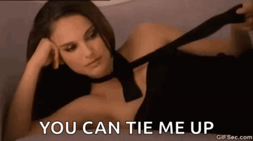 A Woman In A Black Dress Is Laying On A Bed And Tying A Tie . GIF