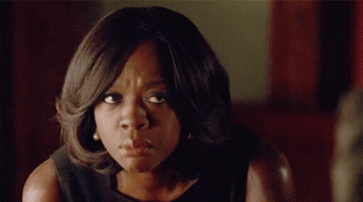 A Woman In A Black Dress Is Making A Funny Face And Looking At The Camera . GIF