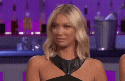 A Woman In A Black Dress Is Making A Funny Face While Sitting In Front Of A Bar . GIF