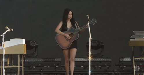 A Woman In A Black Dress Is Playing A Guitar GIF