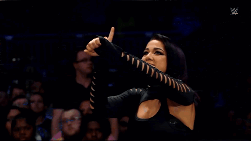 A Woman In A Black Dress Is Screaming In Front Of A Crowd GIF