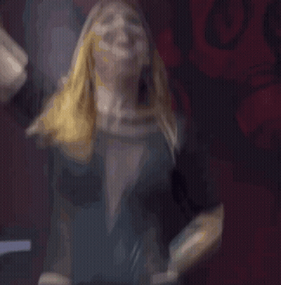 A Woman In A Black Dress Is Screaming With Her Hand In The Air GIF