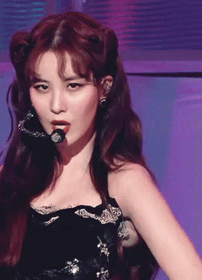 A Woman In A Black Dress Is Singing Into A Microphone On A Stage GIF