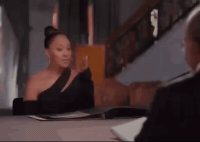 A Woman In A Black Dress Is Sitting At A Table With A Man . GIF