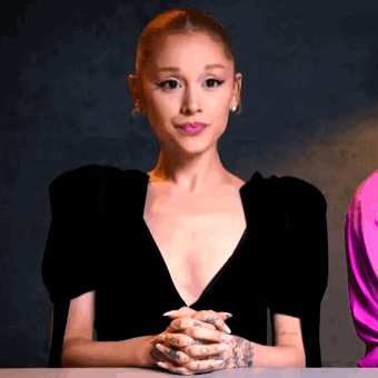A Woman In A Black Dress Is Sitting At A Table With Her Hands Folded In Front Of Her . GIF