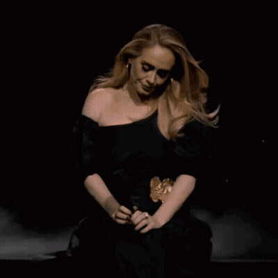 A Woman In A Black Dress Is Sitting Down GIF
