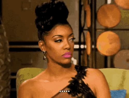 A Woman In A Black Dress Is Sitting In A Chair And Making A Funny Face . GIF