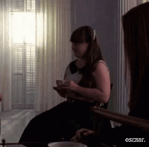 A Woman In A Black Dress Is Sitting In A Chair Holding A Cup Of Tea . GIF
