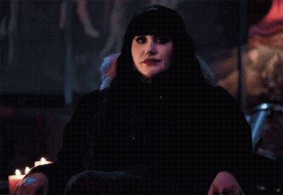 A Woman In A Black Dress Is Sitting In A Chair With Candles In The Background . GIF