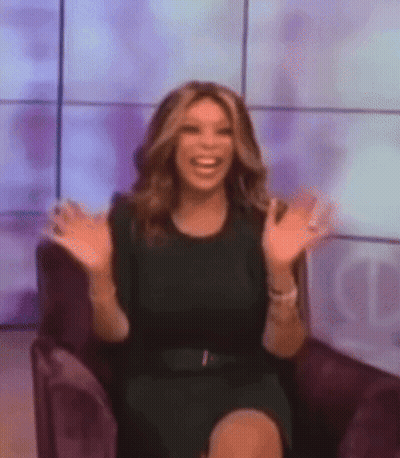 A Woman In A Black Dress Is Sitting In A Chair With Her Arms Outstretched And Smiling . GIF
