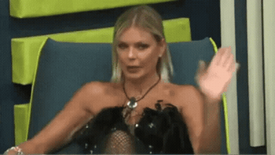 A Woman In A Black Dress Is Sitting In A Chair With Her Hand Up . GIF