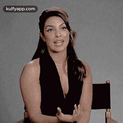 A Woman In A Black Dress Is Sitting In A Director 'S Chair . GIF