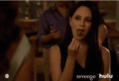 A Woman In A Black Dress Is Sitting In Front Of A Man In A Purple Shirt And A Sign That Says Revenge Hulu GIF