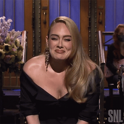 A Woman In A Black Dress Is Sitting In Front Of A Sign That Says Snl On It GIF