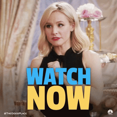 A Woman In A Black Dress Is Sitting In Front Of A Sign That Says Watch Now . GIF