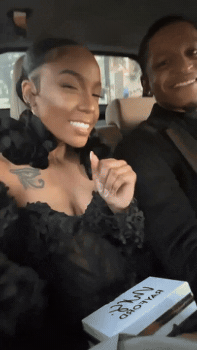 A Woman In A Black Dress Is Sitting Next To A Man In A Car Holding A Box That Says ' Hot Girl ' GIF