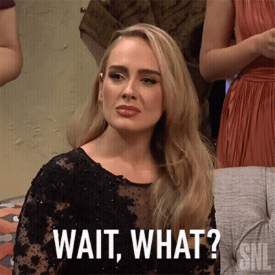 A Woman In A Black Dress Is Sitting On A Couch And Says Wait What . GIF
