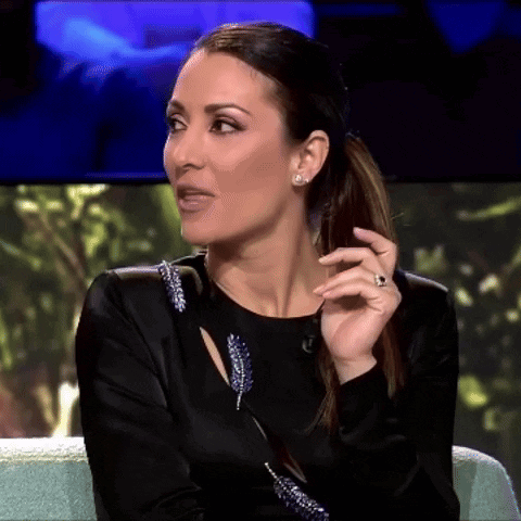 A Woman In A Black Dress Is Sitting On A Couch With Her Hand On Her Face GIF