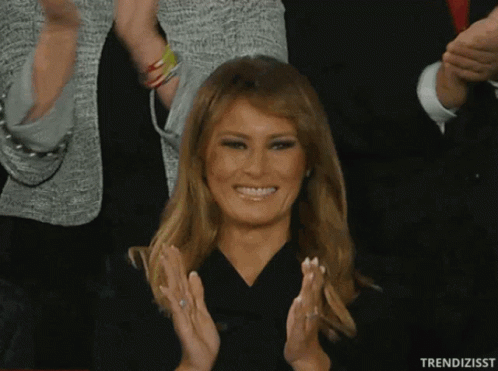 A Woman In A Black Dress Is Smiling And Clapping In Front Of A Crowd GIF