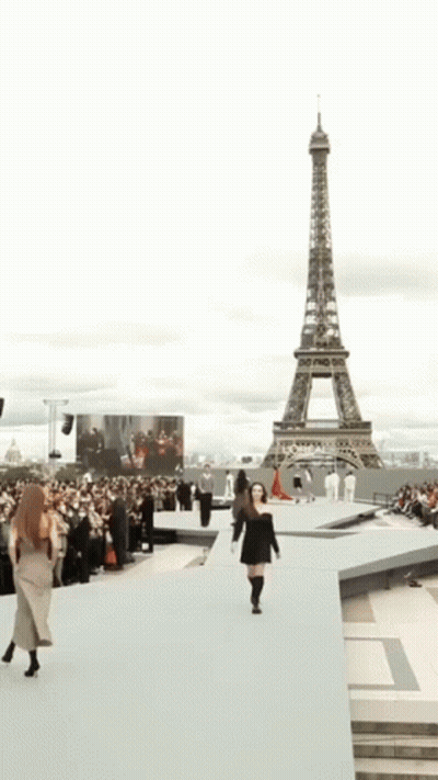 A Woman In A Black Dress Is Smiling And Walking . GIF