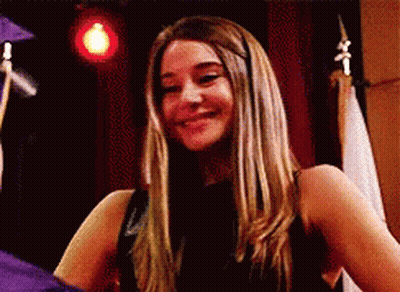A Woman In A Black Dress Is Smiling In Front Of A Man In A Graduation Cap And Gown . GIF