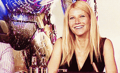 A Woman In A Black Dress Is Smiling In Front Of A Statue GIF