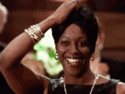 A Woman In A Black Dress Is Smiling With Her Hand On Her Head . GIF