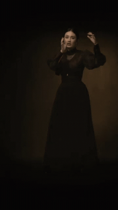 A Woman In A Black Dress Is Standing In A Dark Room With Her Arms Outstretched . GIF