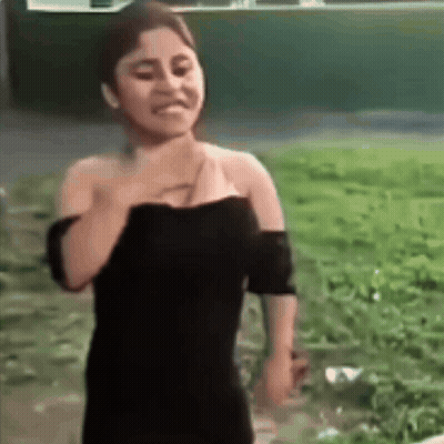 A Woman In A Black Dress Is Standing In A Field With Her Hand On Her Chest . GIF