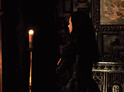 A Woman In A Black Dress Is Standing In Front Of A Candle GIF