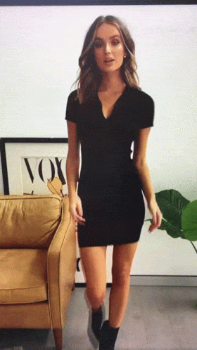 A Woman In A Black Dress Is Standing In Front Of A Couch With A Picture Of A Fox On It GIF