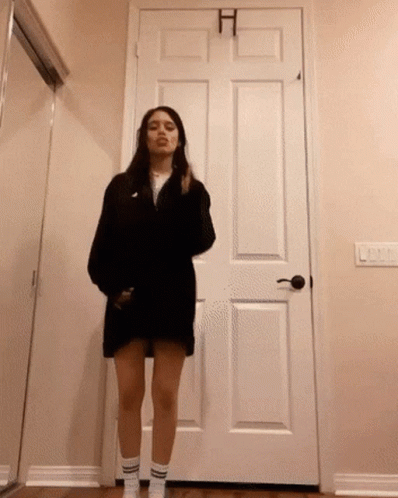 A Woman In A Black Dress Is Standing In Front Of A Door GIF
