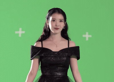 A Woman In A Black Dress Is Standing In Front Of A Green Background GIF