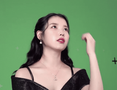 A Woman In A Black Dress Is Standing In Front Of A Green Screen With A Plus Sign On It GIF