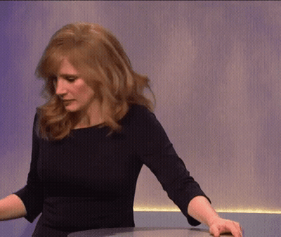 A Woman In A Black Dress Is Standing In Front Of A Purple Wall GIF