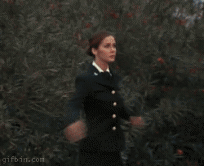 A Woman In A Black Dress Is Standing In Front Of A Red Circle That Says Gifbin.com On It GIF