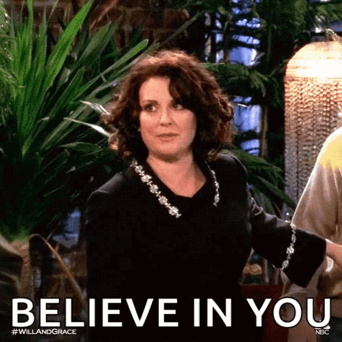 A Woman In A Black Dress Is Standing In Front Of A Sign That Says Believe In You GIF