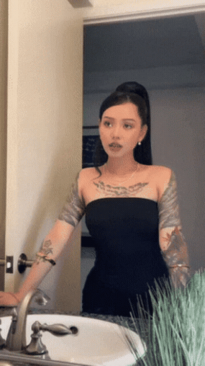 A Woman In A Black Dress Is Standing In Front Of A Sink GIF