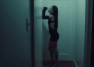 A Woman In A Black Dress Is Standing In Front Of A White Door GIF