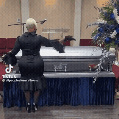 A Woman In A Black Dress Is Standing Next To A Coffin In A Church . GIF