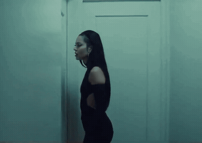 A Woman In A Black Dress Is Standing Next To A Door In A Dark Room . GIF
