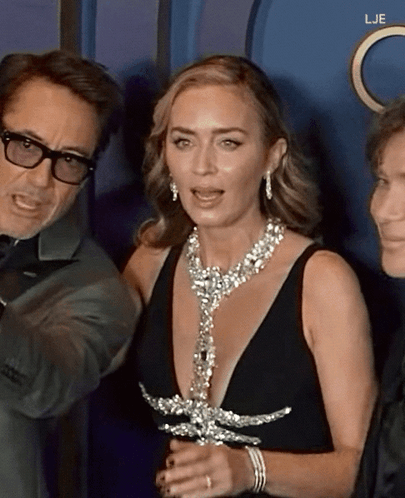 A Woman In A Black Dress Is Standing Next To A Man In Glasses GIF
